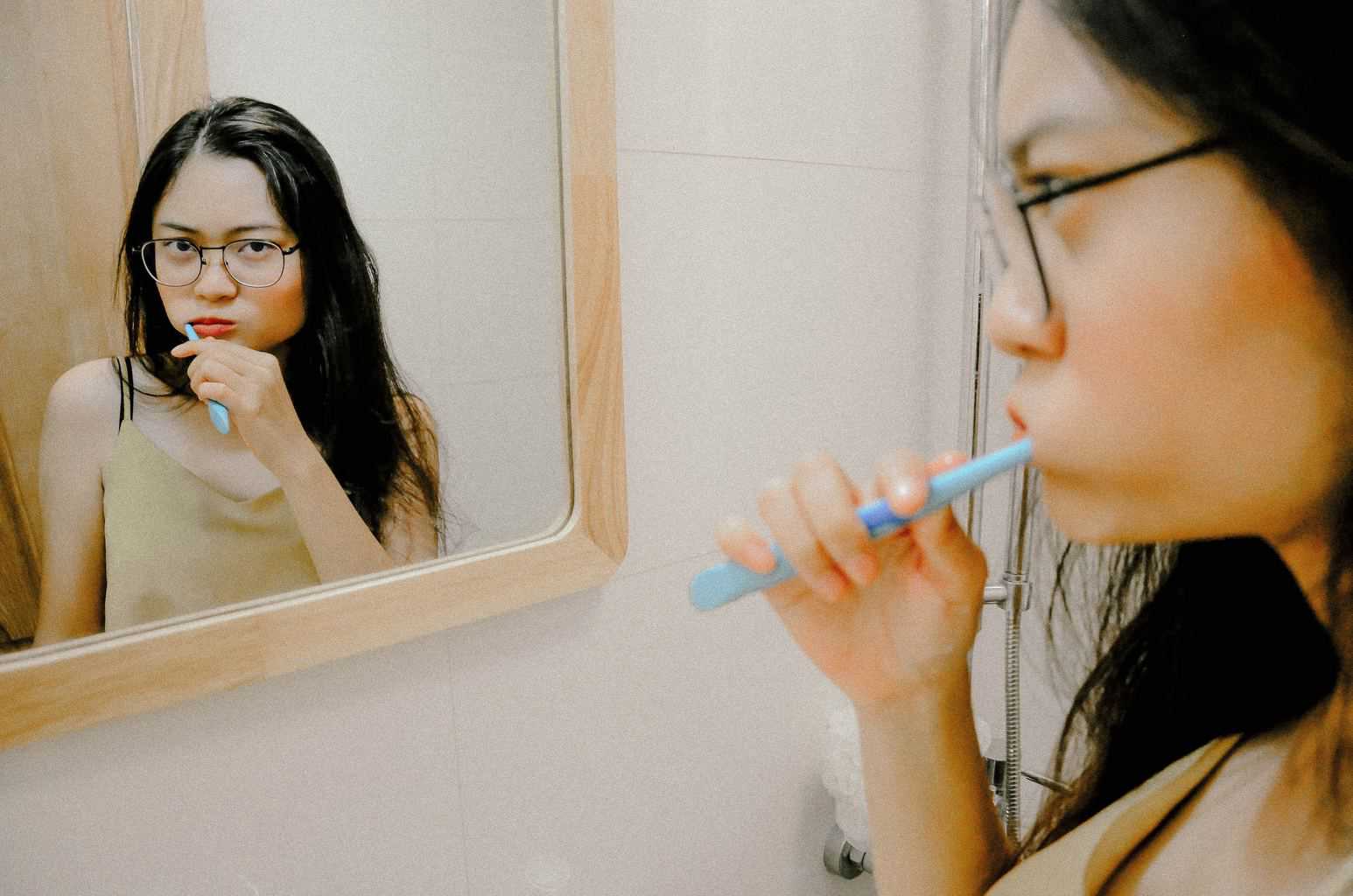 Mujer cepilla los dientes frente al espejo