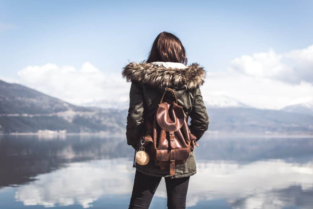mujer de pie frente al lago con una mochila de cuero